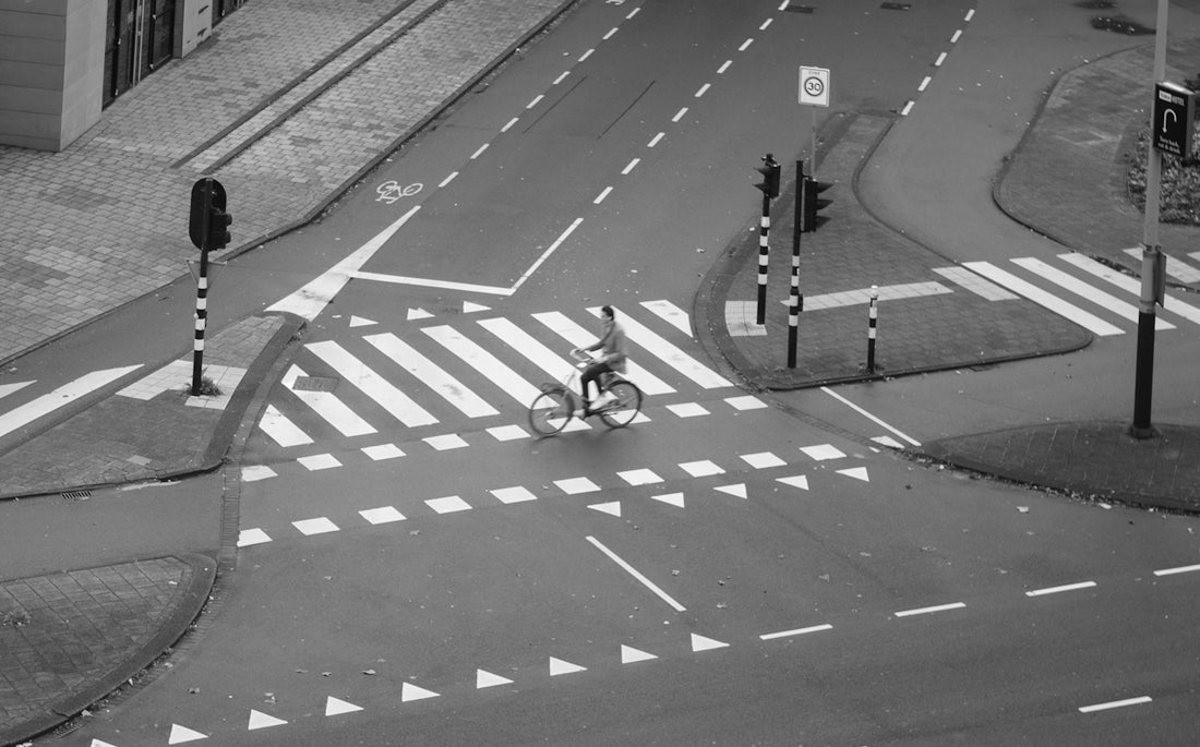 grayscale photo of man riding city bike passing by pedestrian lane