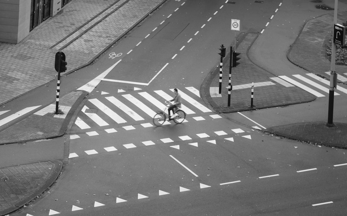 grayscale photo of man riding city bike passing by pedestrian lane