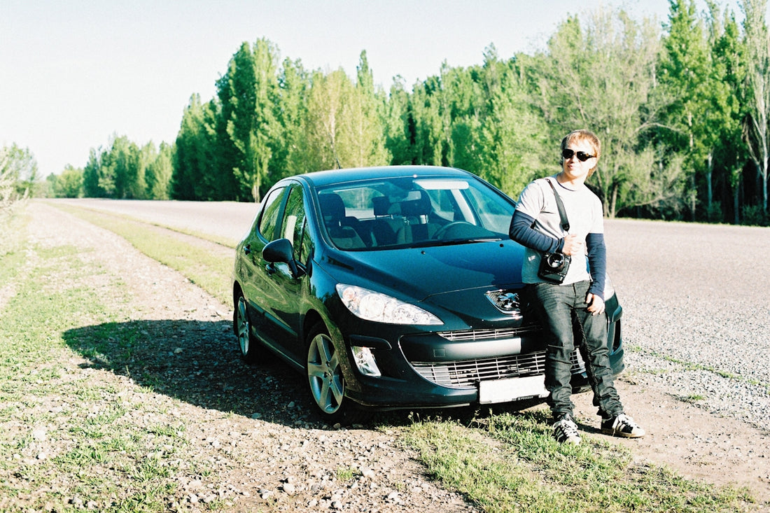 a man standing next to a car on a dirt road