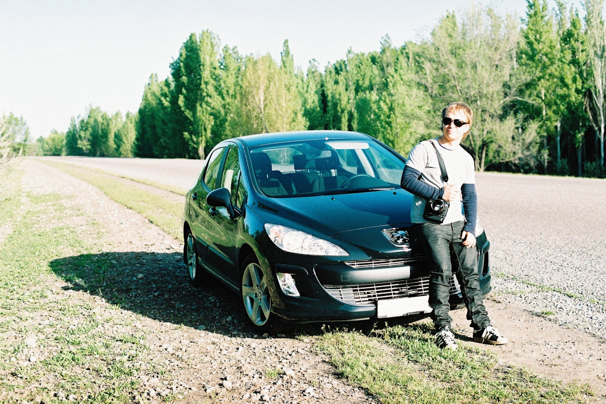 a man standing next to a car on a dirt road