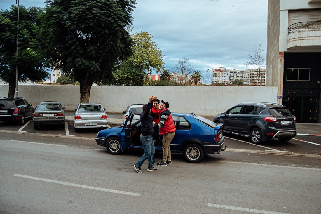 a couple of people standing in a parking lot with cars and trees