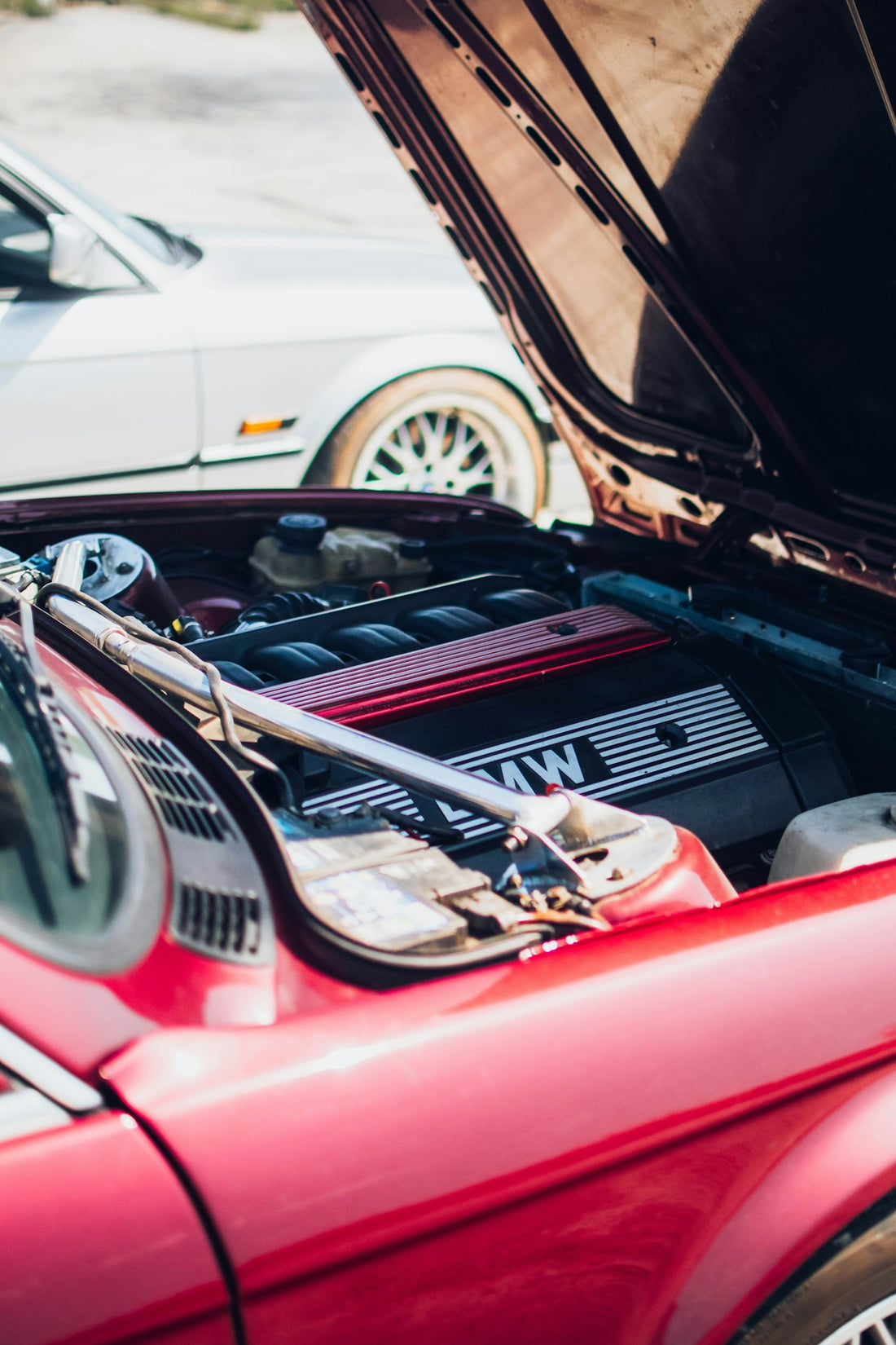 a red car with its hood open next to a white car