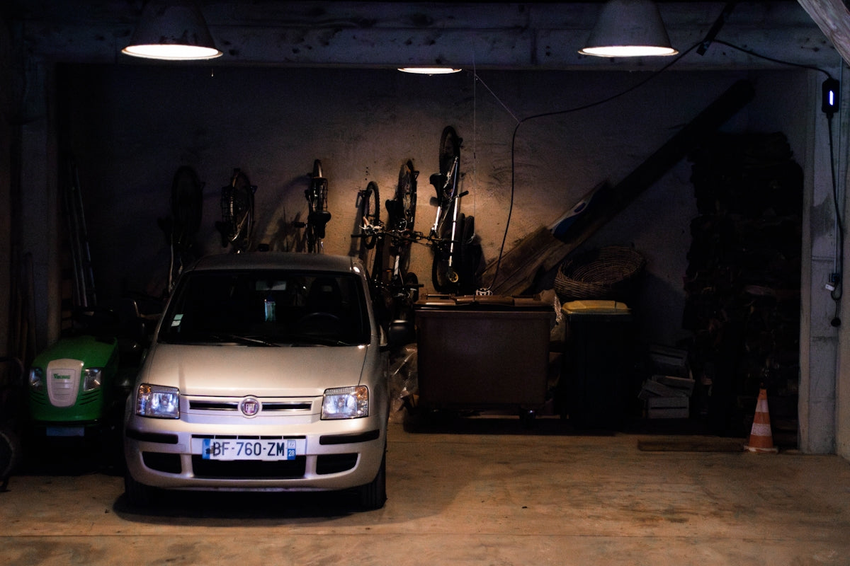 A car is parked inside a dark, cluttered garage.