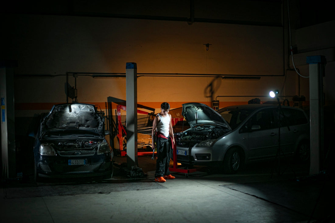 Mechanic working on cars in a dimly lit garage.