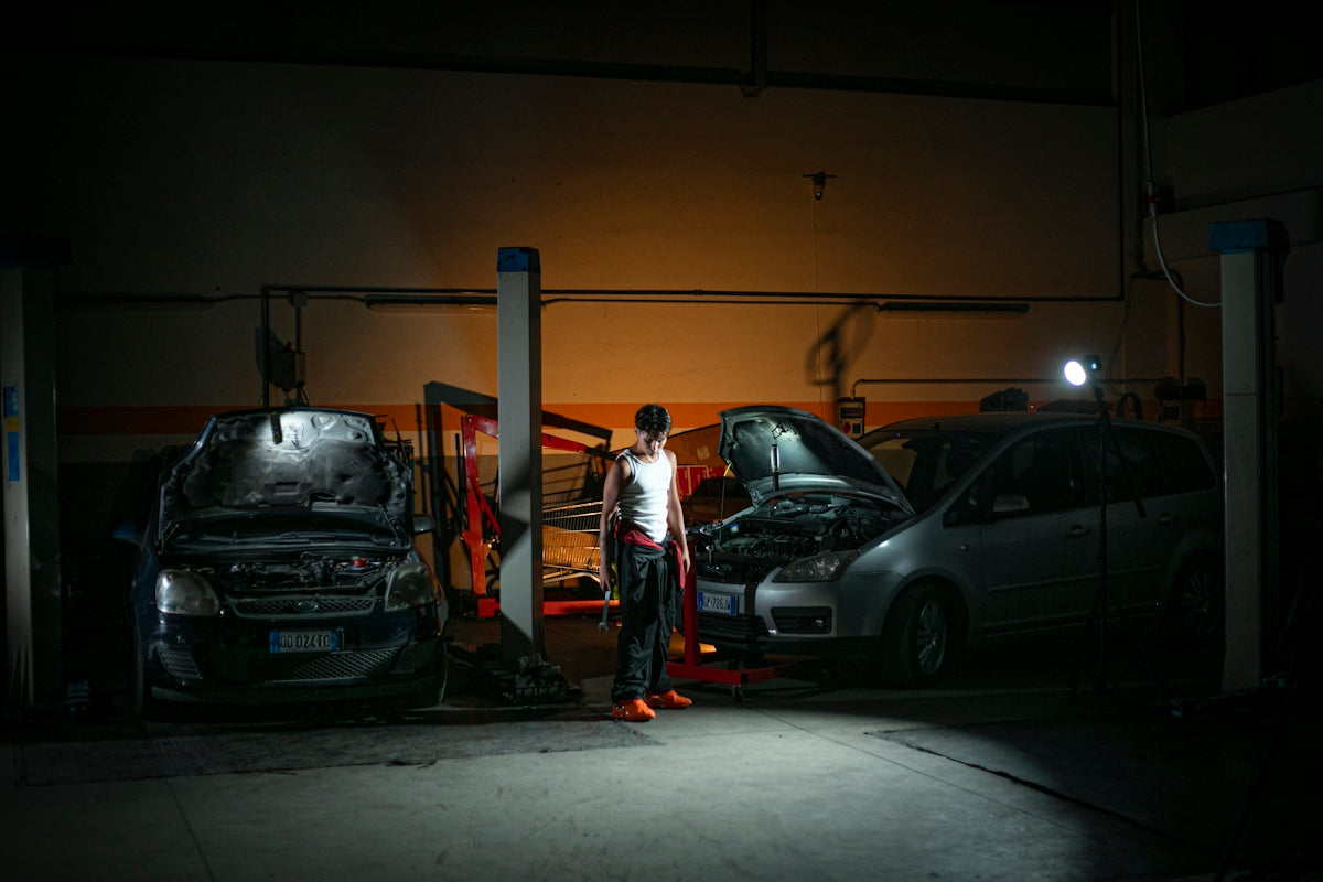 Mechanic working on cars in a dimly lit garage.