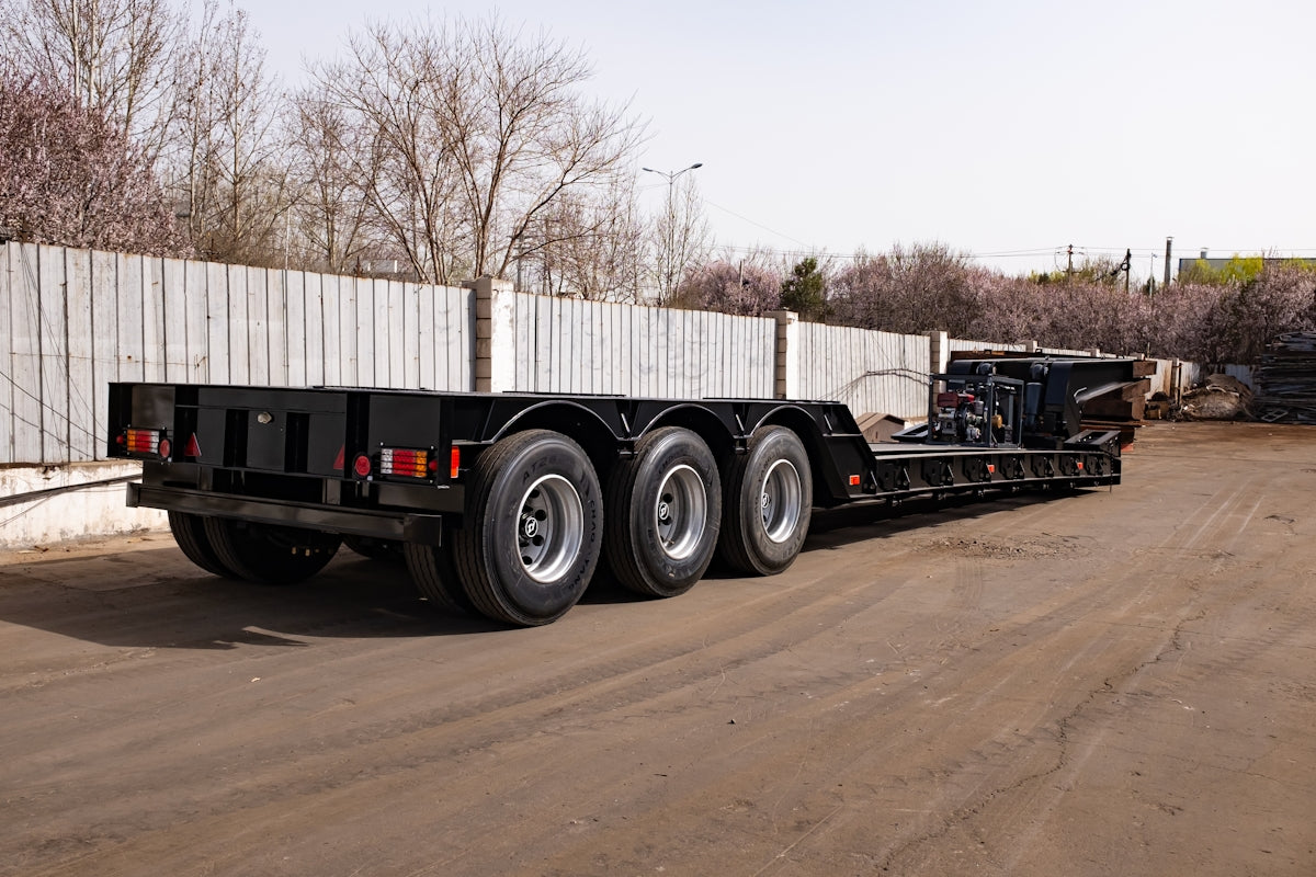 A black triple axle trailer parked on pavement.