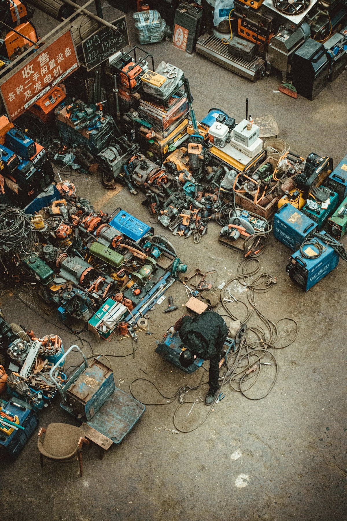 Man works with welding equipment in a cluttered workshop.